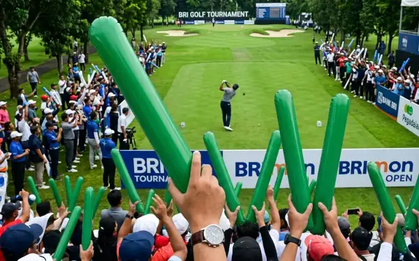 Balon tepuk Batang berwarna hijau diangkat penonton saat menyaksikan pertandingan golf di lapangan terbuka.