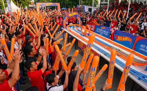 Kerumunan penonton membawa balon tepuk oranye saat menyaksikan perlombaan Hot Wheels di tengah suasana meriah.