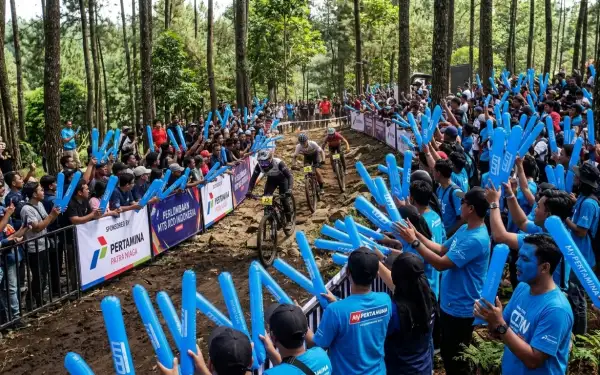 Penonton memberikan semangat kepada peserta lomba sepeda menggunakan balon tepuk berwarna biru di sepanjang lintasan.