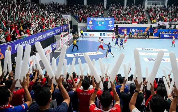 Ribuan suporter memenuhi tribun sambil mengangkat balon tepuk Dharmasraya berwarna putih untuk mendukung pertandingan bola tangan di arena indoor.