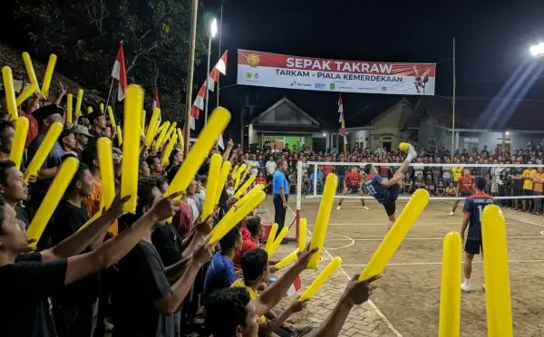 Suporter membawa balon tepuk kuning sambil menyaksikan pertandingan sepak takraw pada acara tarkam.