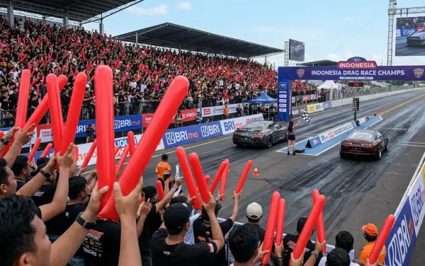 Suporter menggunakan balon tepuk merah saat menyaksikan balap drag mobil.