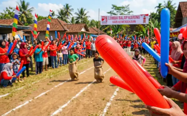 Warga memegang balon panjang berwarna merah dan biru saat memeriahkan lomba balap karung.