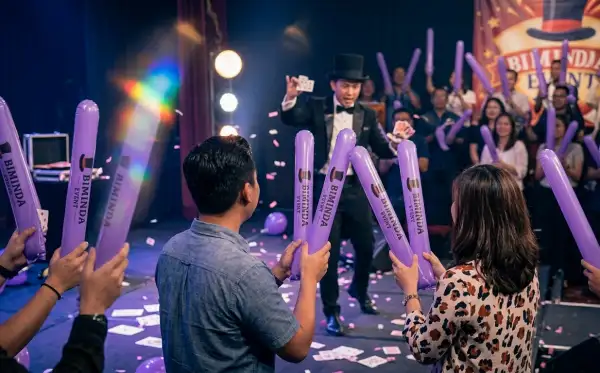 Penonton memegang balon ungu sambil menikmati pertunjukan sulap di dalam ruangan.