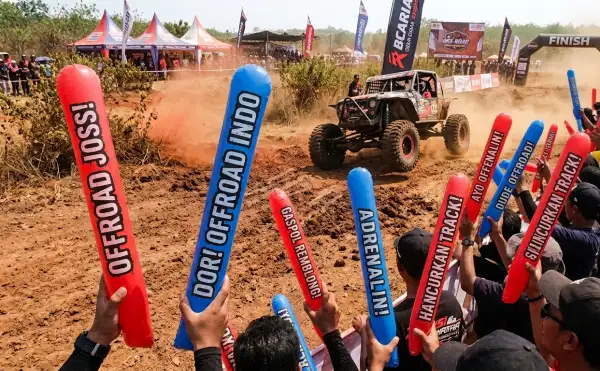 Penonton mengangkat balon tepuk berwarna merah dan biru saat menyaksikan ajang offroad di area lintasan berlumpur.