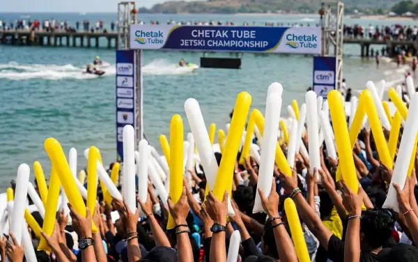Penonton membawa balon kuning dan putih sambil menikmati keseruan lomba jetski yang berlangsung di kawasan tepi pantai