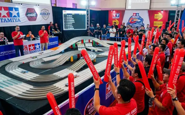 Para penonton membawa balon merah sambil menyaksikan perlombaan mobil mainan Tamiya yang berlangsung di dalam area acara