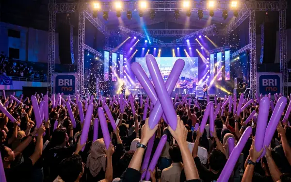 Suasana konser musik dengan penonton memegang balon tepuk berwarna ungu.