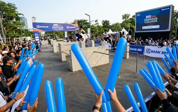 Penonton membawa balon tepuk lahat berwarna biru saat menyaksikan acara parkour di area terbuka.