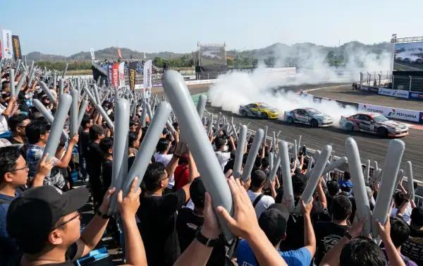 Penonton menyaksikan aksi mobil drift sambil mengangkat balon tepuk berwarna abu-abu.