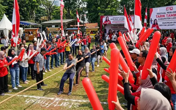 Peserta memegang balon tepuk berwarna merah dan putih saat memeriahkan perlombaan tarik tambang.