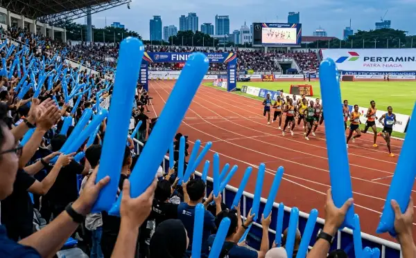 Penonton mengangkat balon panjang berwarna biru saat menyaksikan perlombaan lari di stadion.