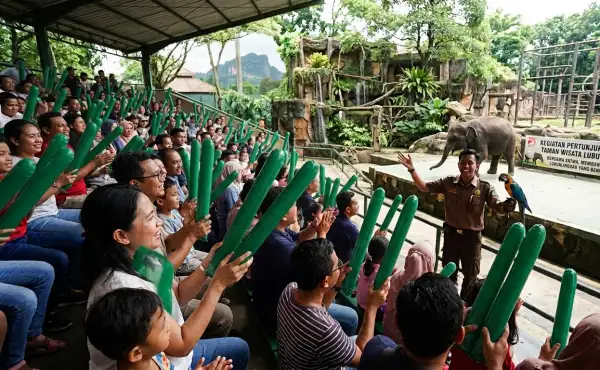Penonton membawa balon tepuk berwarna hijau saat menikmati pertunjukan satwa di kebun binatang.