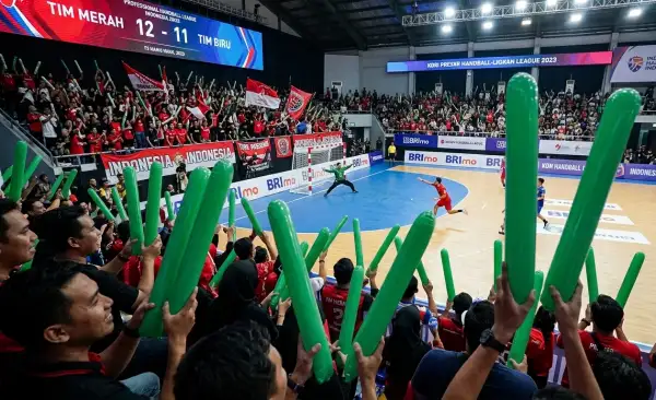 Suporter mengangkat balon tepuk berwarna hijau saat menyaksikan pertandingan bola tangan di dalam arena