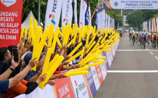 Ribuan penonton di tepi lintasan melambaikan balon tepuk kuning untuk memberikan semangat kepada para pembalap sepeda yang melintas.
