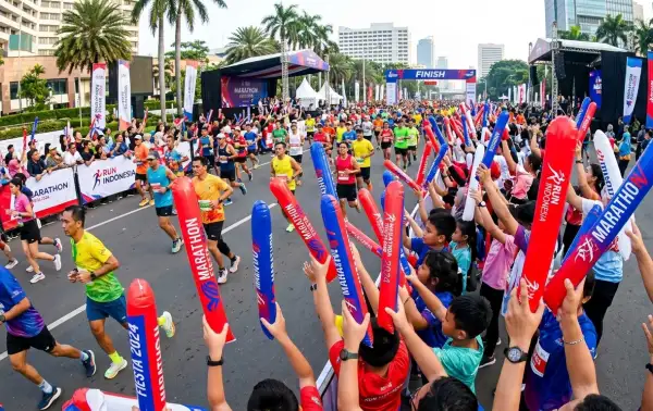Penonton sedang menyemangati peserta lomba lari maraton di area jalan raya.