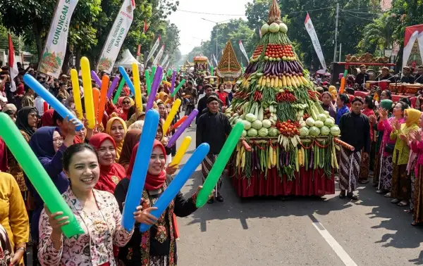 Warga membawa balon tepuk warna-warni sambil menyaksikan arak-arakan gunungan sayur dalam festival budaya.