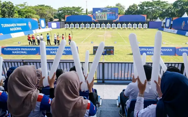 Penonton menggunakan balon tepuk Pakpak Bharat saat menyaksikan perlombaan panahan di lapangan terbuka.