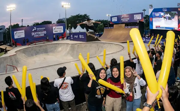 Penonton memeriahkan acara skateboard dengan mengangkat balon tepuk berwarna kuning.