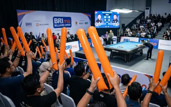 Penonton mengangkat balon tepuk oranye untuk memberikan dukungan pada pertandingan biliard di dalam arena.
