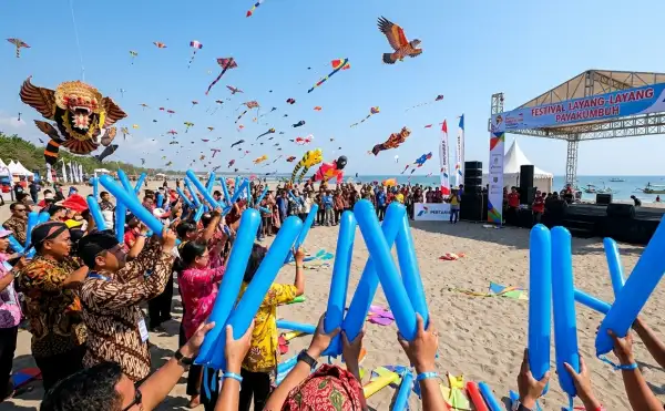 Balon tepuk Payakumbuh biru memeriahkan Festival Layang-Layang di tepi pantai dengan langit penuh layangan.