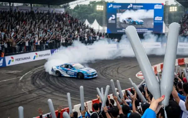 Penonton mengangkat balon tepuk berwarna putih saat menyaksikan aksi mobil drift di lintasan.