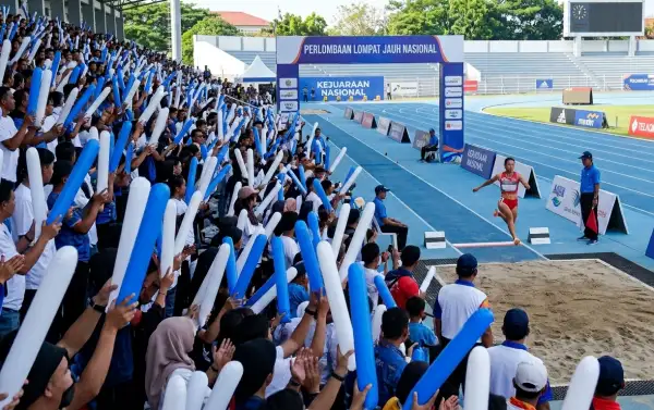 Penonton menggunakan balon tepuk Prabumulih berwarna biru dan putih untuk memberikan dukungan pada kejuaraan nasional lompat jauh di stadion.