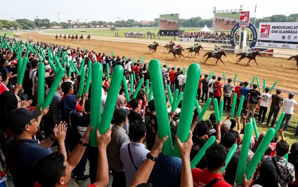 Ribuan penonton di tribun menyaksikan perlombaan pacuan kuda di arena balap.
