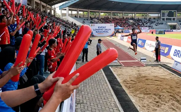 Penonton menggunakan balon tepuk merah saat mendukung peserta lomba lompat jauh di stadion