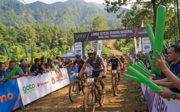 Penonton menyemangati peserta lomba sepeda gunung dengan balon tepuk hijau di jalur pegunungan.