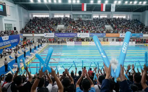 Penonton menyemangati lomba renang dengan Balon Tepuk Seruyan berwarna biru di tribun.