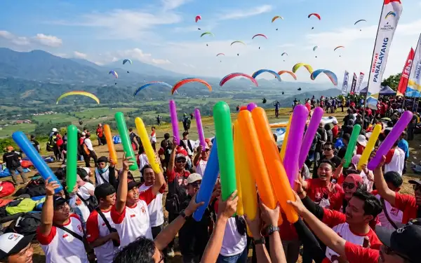 Peserta festival paralayang mengangkat balon tepuk warna-warni untuk memeriahkan suasana.