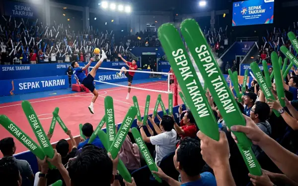 Penonton sedang memeriahkan pertandingan sepak takraw di arena.