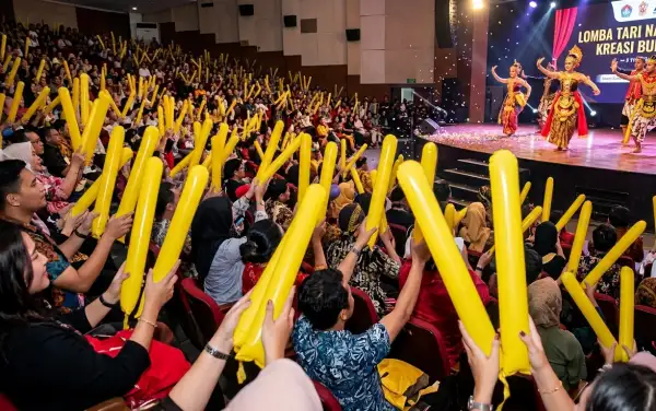 Penonton memegang balon tepuk kuning saat menyaksikan pertunjukan lomba tari di dalam gedung.