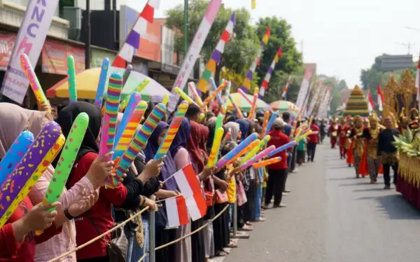 Warga membawa balon tepuk warna-warni sambil menyaksikan kemeriahan karnaval gunungan di sepanjang jalan.