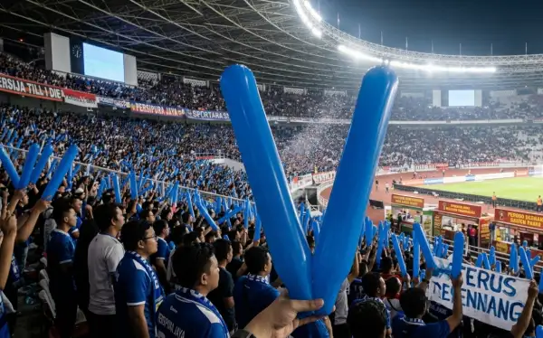 Suporter mendukung pertandingan sepak bola di dalam stadion.