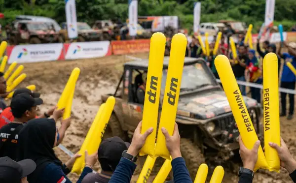 Penonton membawa balon tepuk berwarna kuning sambil menyaksikan aksi kendaraan dalam ajang offroad.