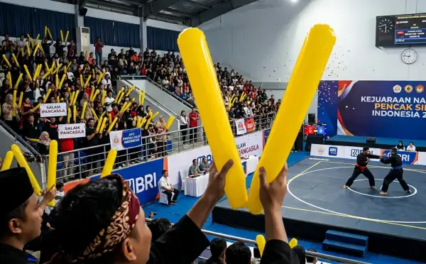 Penonton membawa balon tepuk berwarna kuning saat mendukung pertandingan pencak silat di dalam arena.