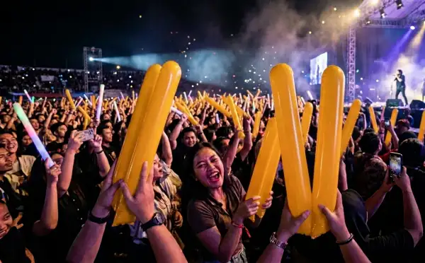 Suasana konser musik semakin meriah dengan penonton yang mengangkat balon tepuk berwarna kuning.