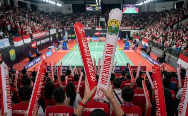 Balon promosi Manado berupa balon tepuk bertuliskan dukungan untuk menyemarakkan pertandingan badminton di dalam arena olahraga.