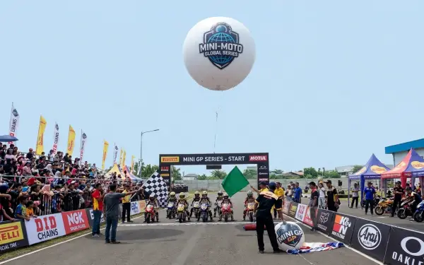 Di atas arena perlombaan motor mini dengan logo sponsor, penonton, dan peserta balap.